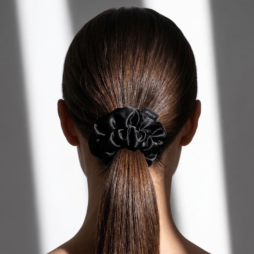 The back of a woman's head with her brown hair in a ponytail held by a black silk scrunchie.