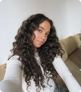 Person with long curly hair taking a selfie on a couch.