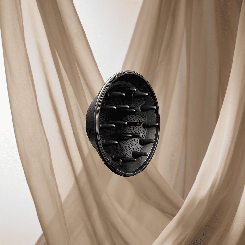 A close-up of a black hair dryer diffuser attachment against a backdrop of flowing beige fabric.