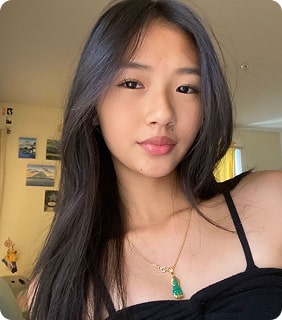 Young woman with long hair wearing a black top and necklace, indoors.