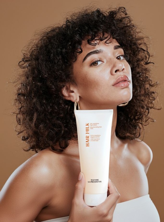 Person holding a hair milk product against a brown background.