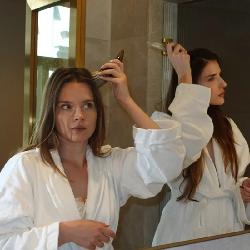 Woman in a bathrobe brushing her hair in front of a mirror.