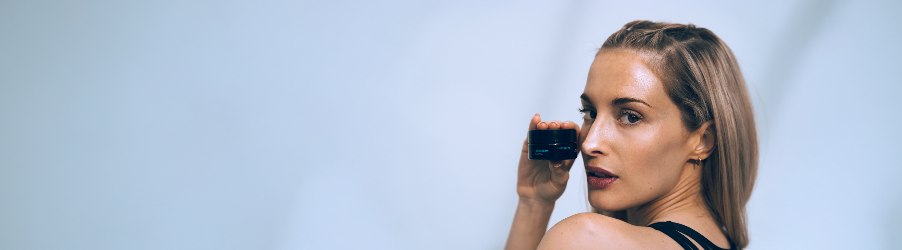 Person holding a small black container against a light blue background.