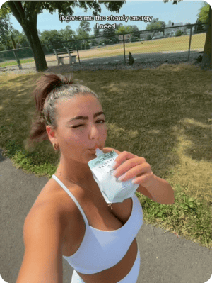 Person in athletic wear drinking from a pouch outdoors.