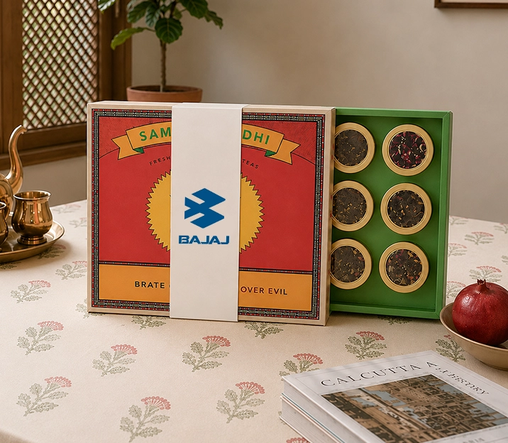 A Bajaj branded gift box of assorted teas sits on a floral patterned tablecloth.