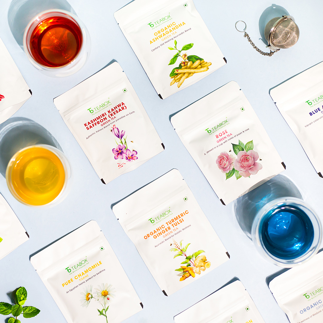 Assorted tea packets and cups with different colored teas on a light background.