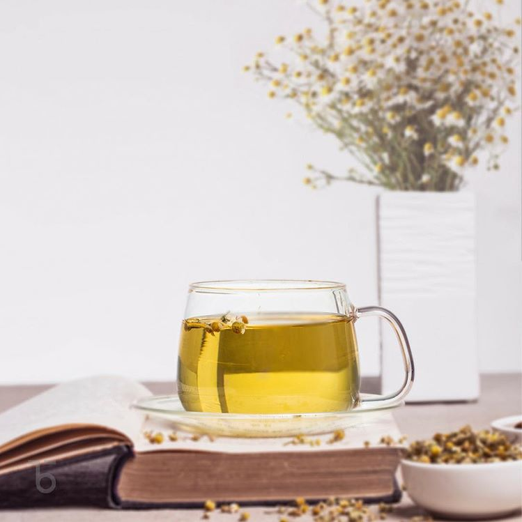 Glass cup of herbal tea on a book, with flowers in the background.