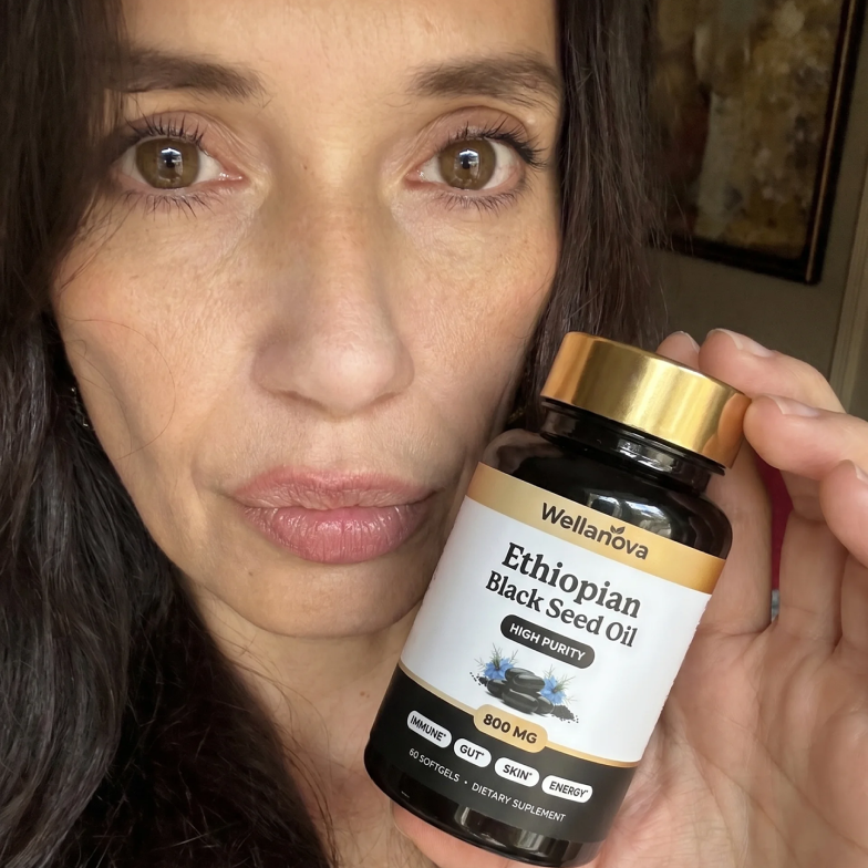 A woman holds a bottle of Wellanova Ethiopian Black Seed Oil softgels up to the camera.