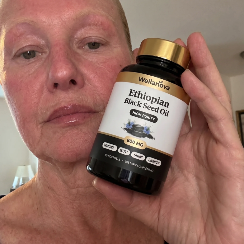 A woman with reddish skin holds a bottle of Wellanova Ethiopian Black Seed Oil softgels.