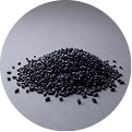 A circular photo of a small pile of black grains, possibly barley, on a grey textured surface.