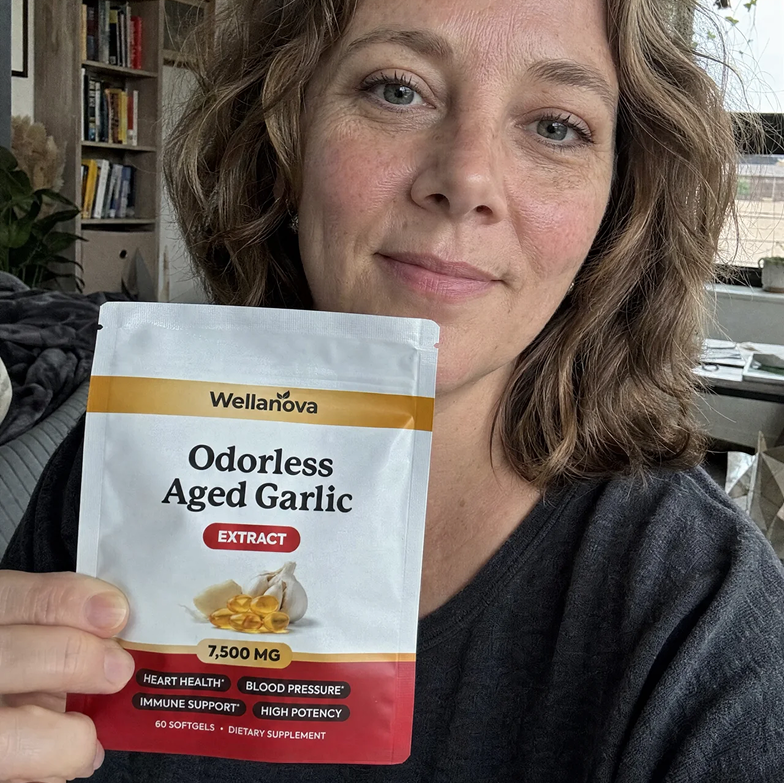 A woman holds up a pouch of Wellanova Odorless Aged Garlic Extract supplement.