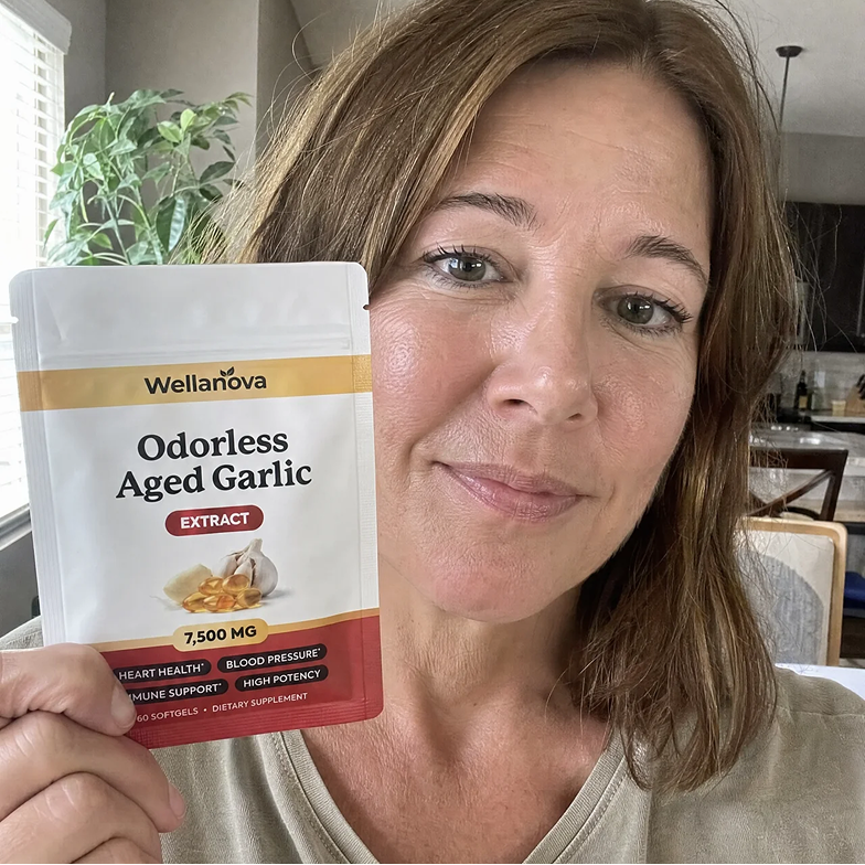 A woman with light brown hair holds up a white and red pouch of Wellanova Odorless Aged Garlic.