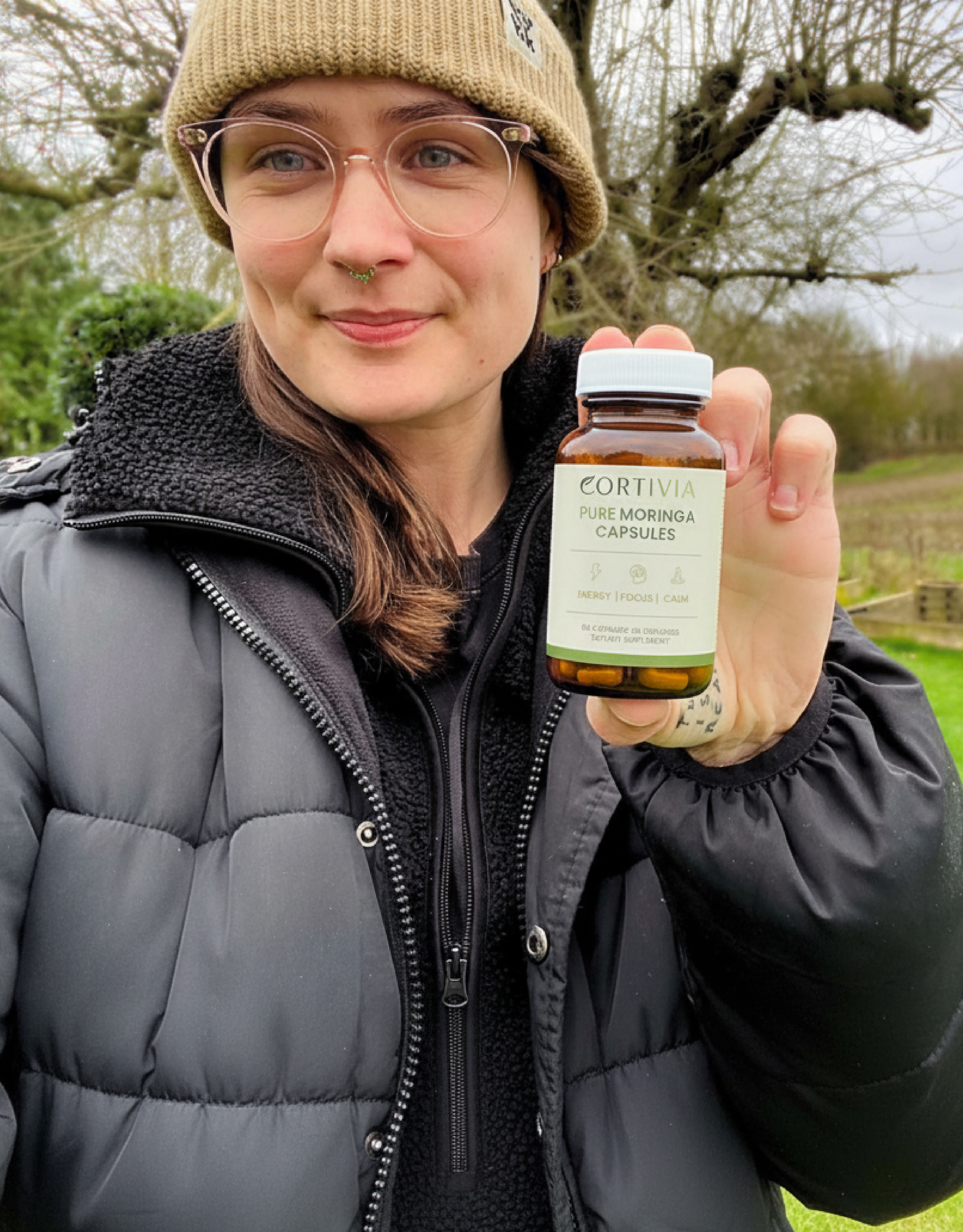 Person outdoors holding a bottle of Pure Moringa Capsules.