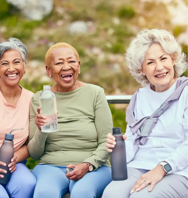 Three smiling women sitting outdoors holding water bottles.