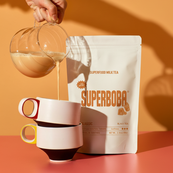 Hand pours tea into stacked mugs beside a packaged tea bag.