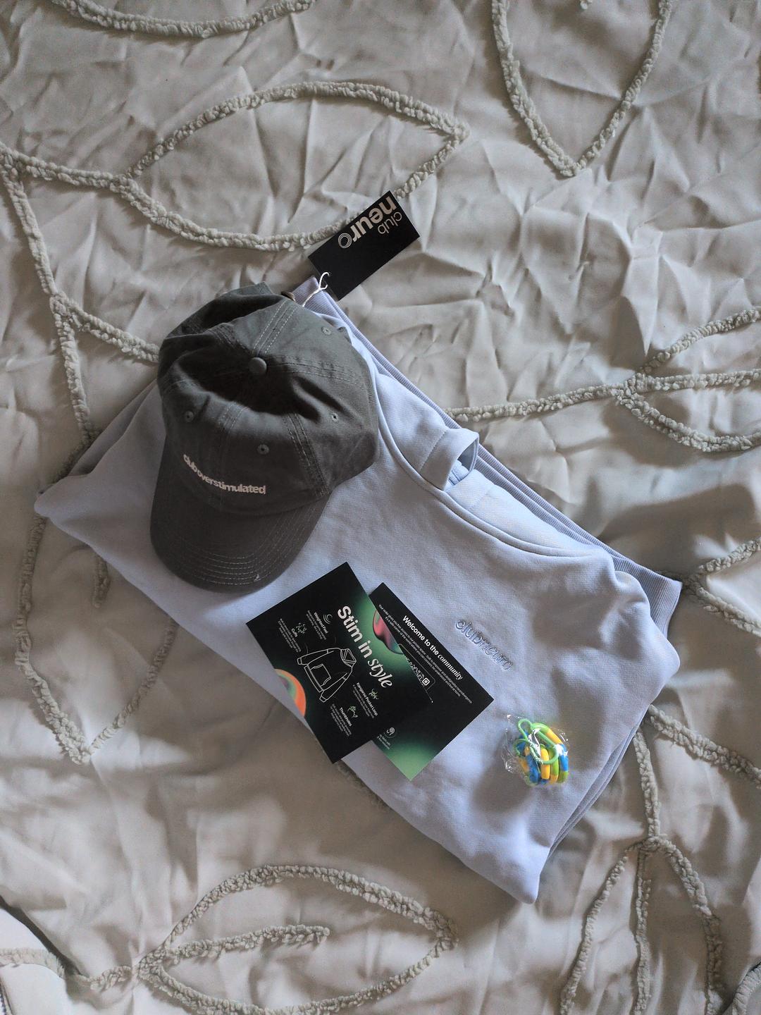 A flat lay of a folded sweatshirt, a baseball cap, cards, and a small toy on a bedspread.