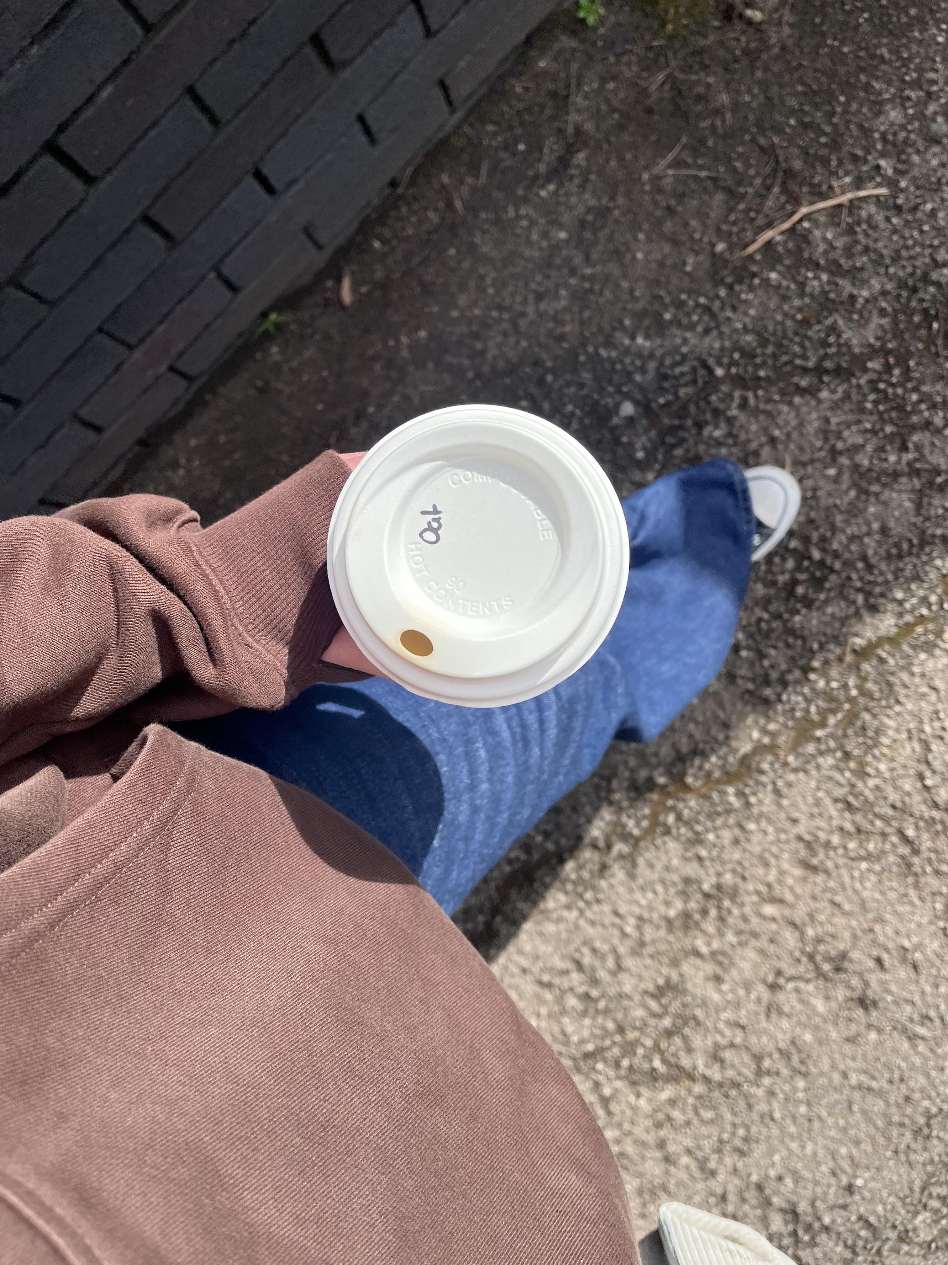 A top-down view of a person holding a white coffee cup while standing on a sidewalk.