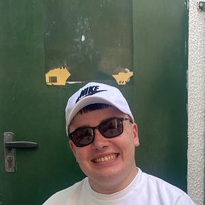 A young man in a white Nike cap and sunglasses smiles for the camera in front of a green door.