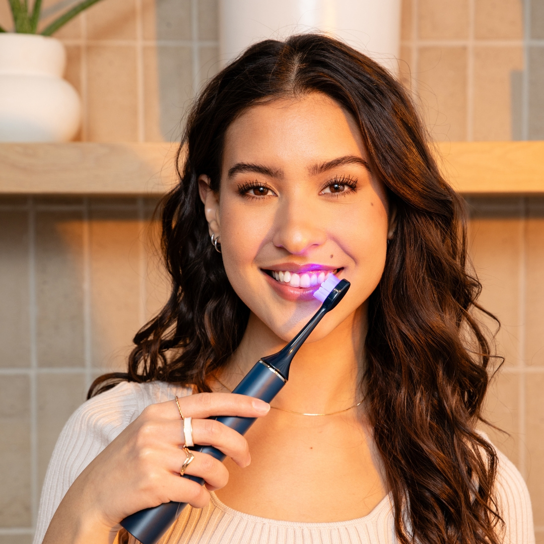 Person holding a toothbrush with a blue light near their teeth.