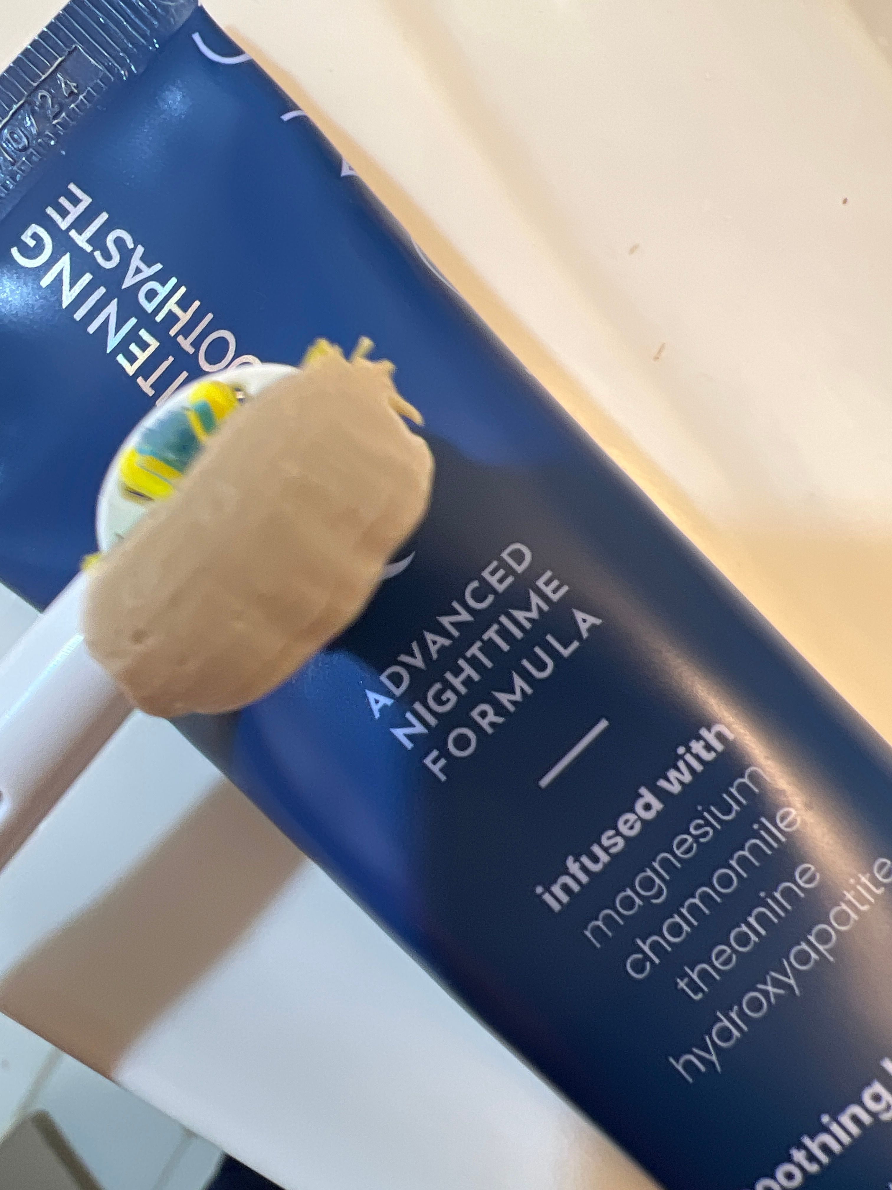 Toothpaste on a toothbrush next to a blue tube labeled 'Advanced Nighttime Formula.'