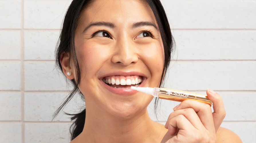 Person smiling while using a dental pen with a gold handle.