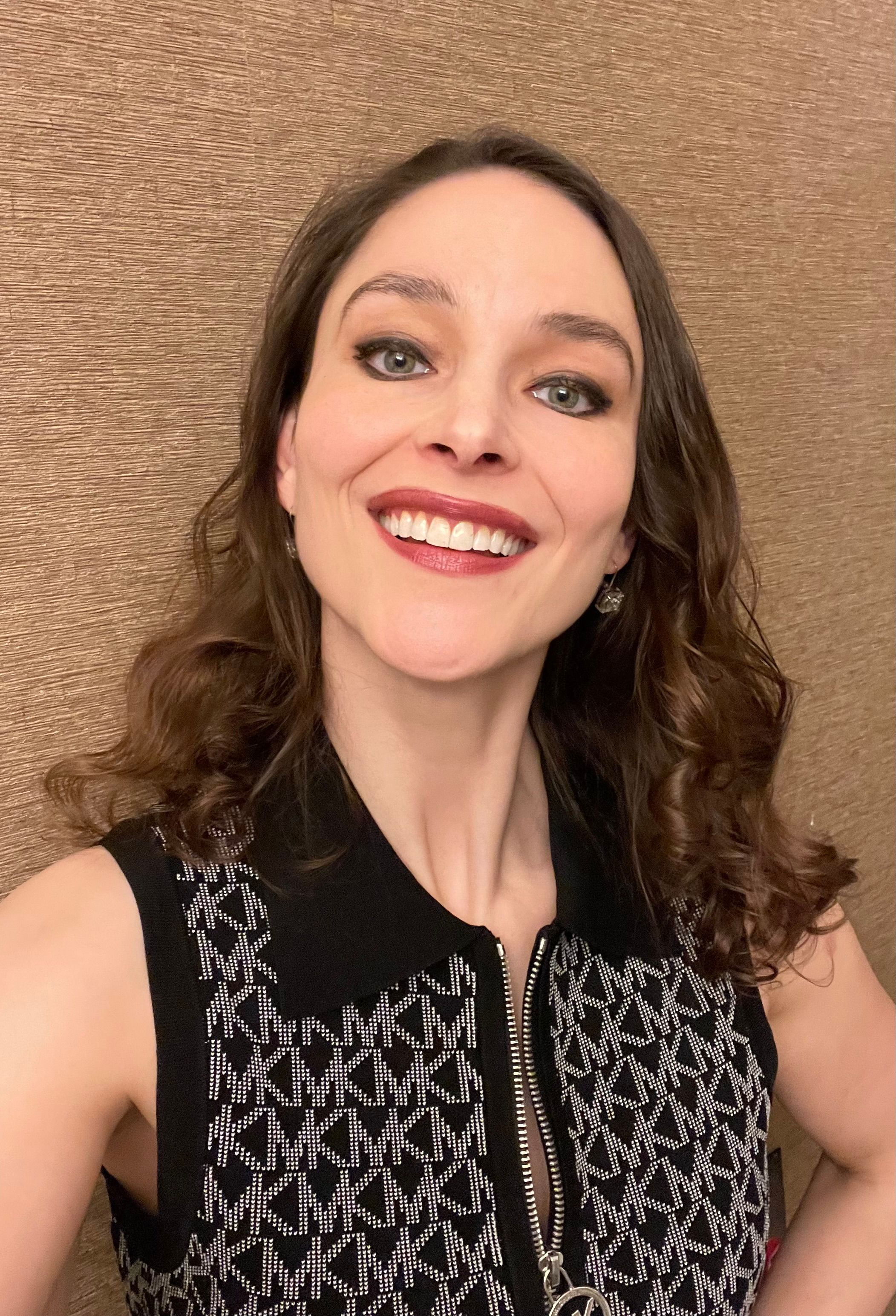 Smiling woman with curly hair and patterned sleeveless top.