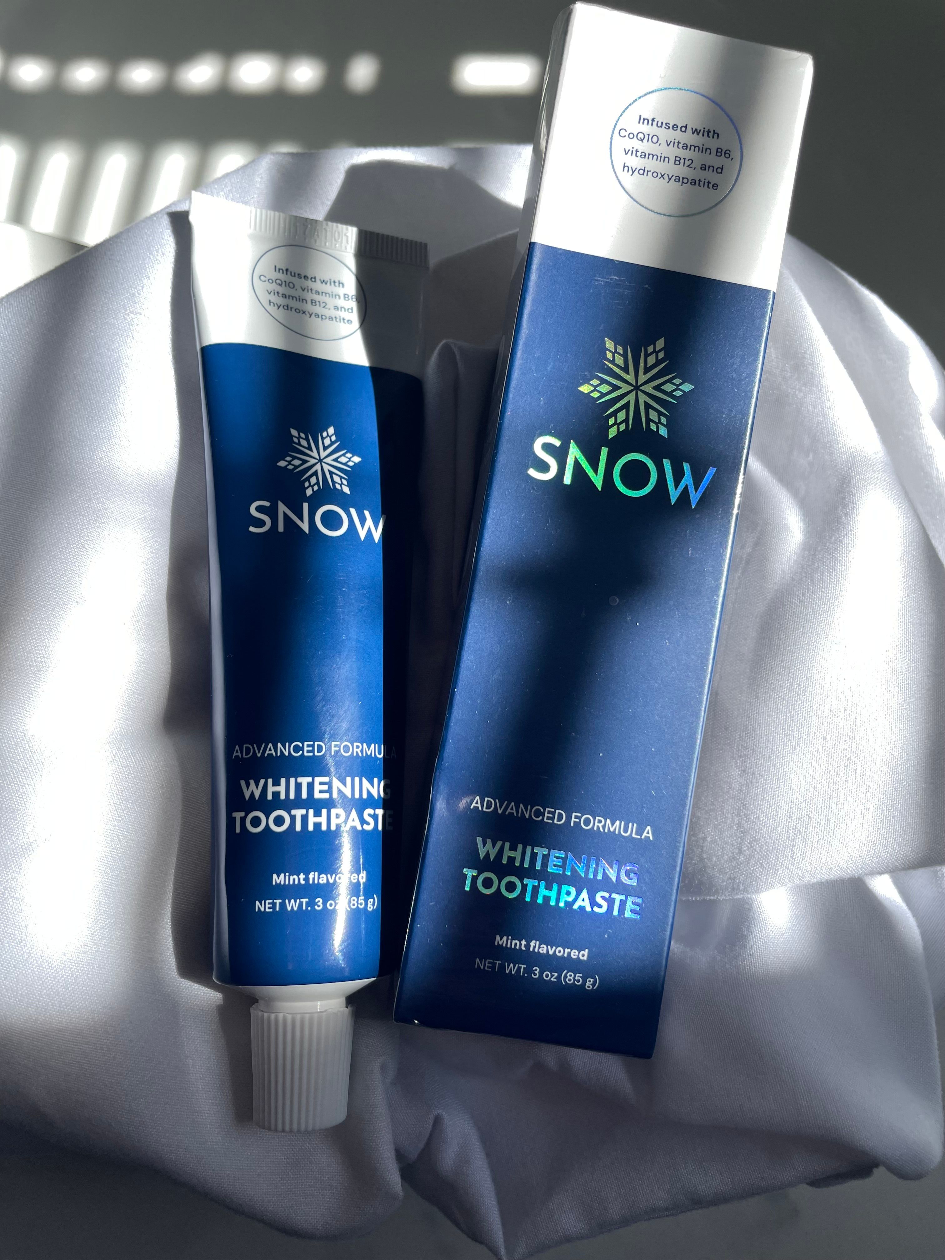 Snow whitening toothpaste tube and box on a white cloth.