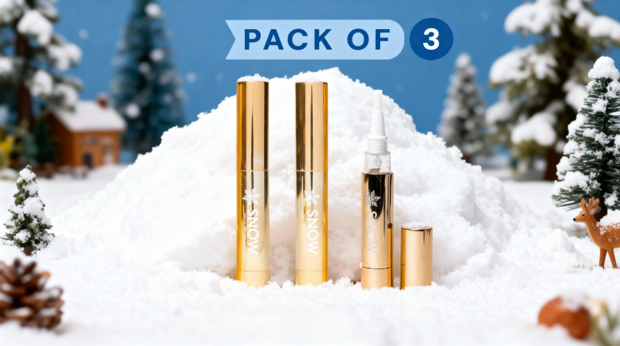 Three gold cosmetic tubes in snow with trees and a house in the background.