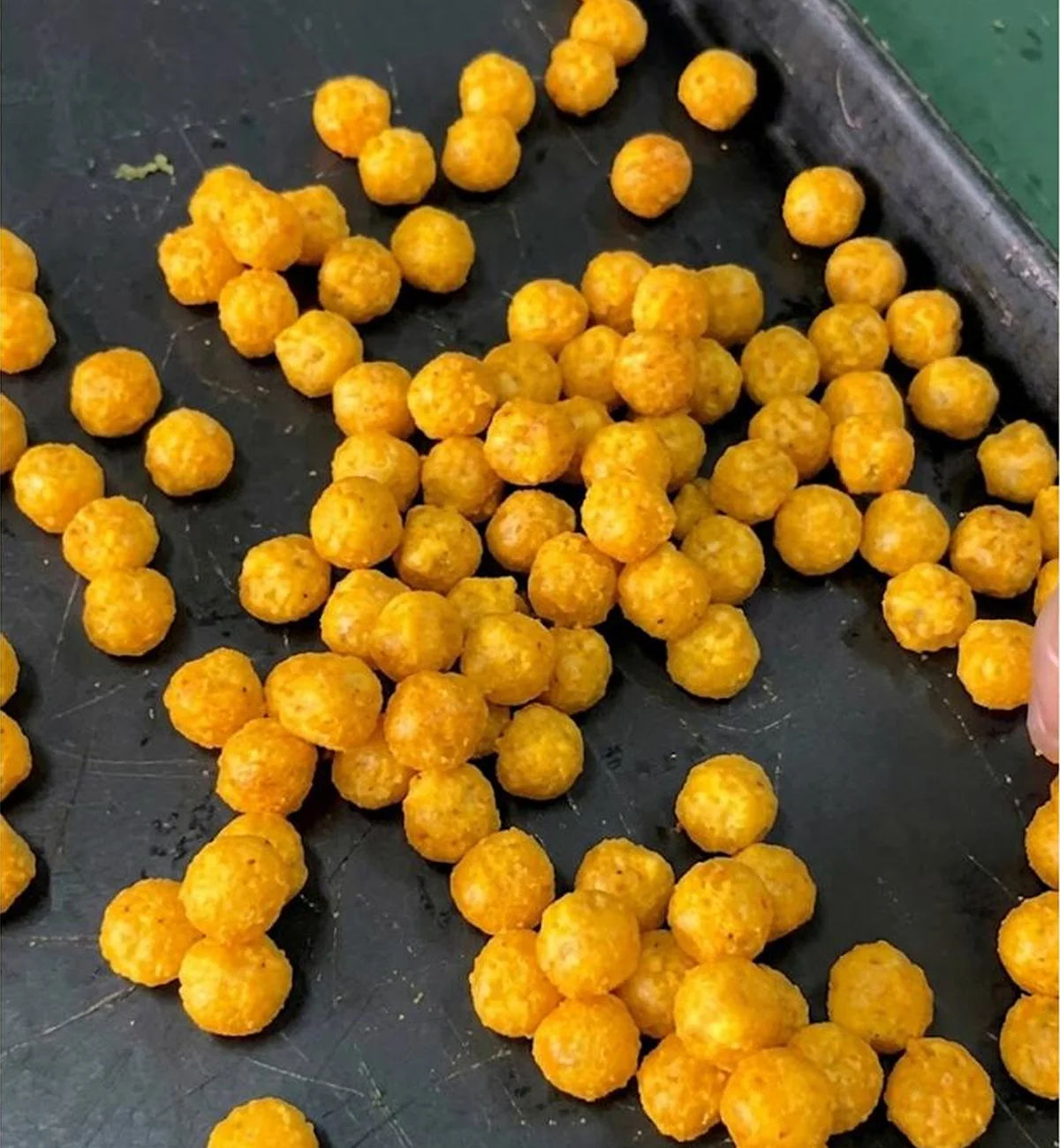 A close-up of small, round, orange, puffy snacks on a dark tray.
