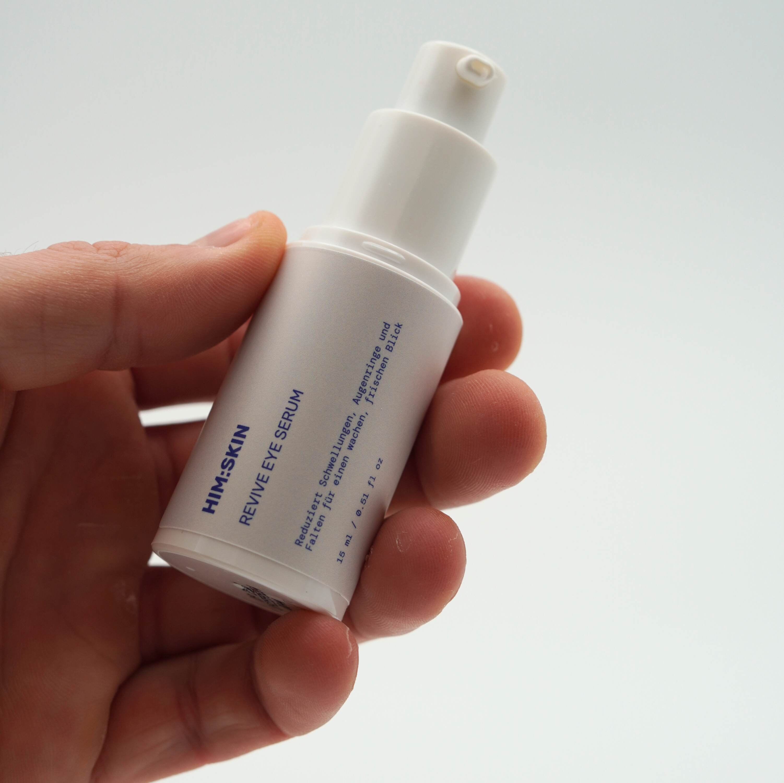 Hand holding a white bottle labeled 'HIM+SKIN REVIVE EYE SERUM'.