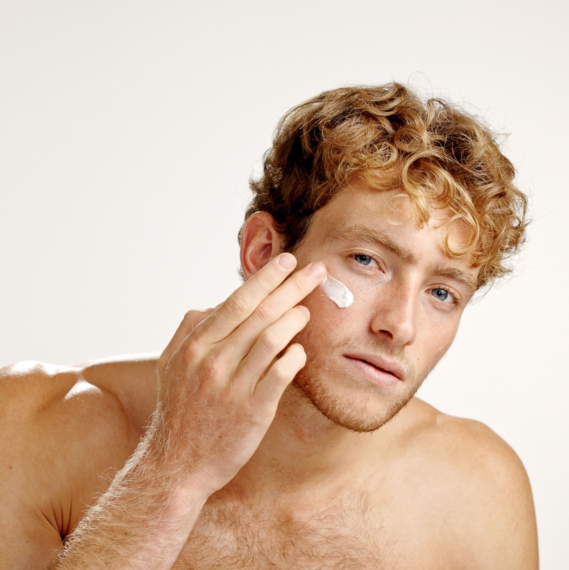 Person applying cream to face with fingers.