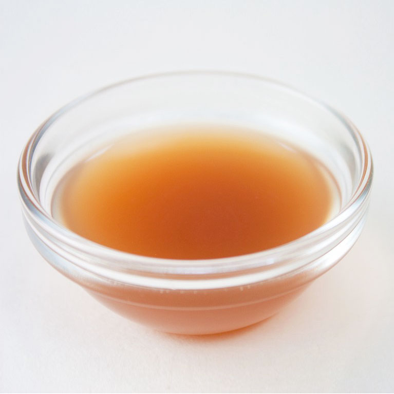 A small glass bowl filled with brown liquid on a white background.