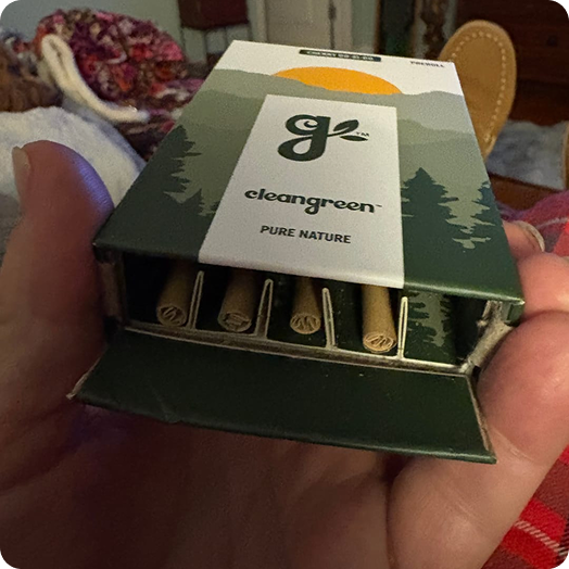 A hand holding an open green and white box of 'cleangreen' brand pre-rolls.