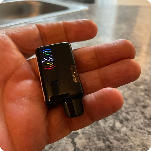 A small black electronic device with a colorful lit display resting in the palm of a hand.