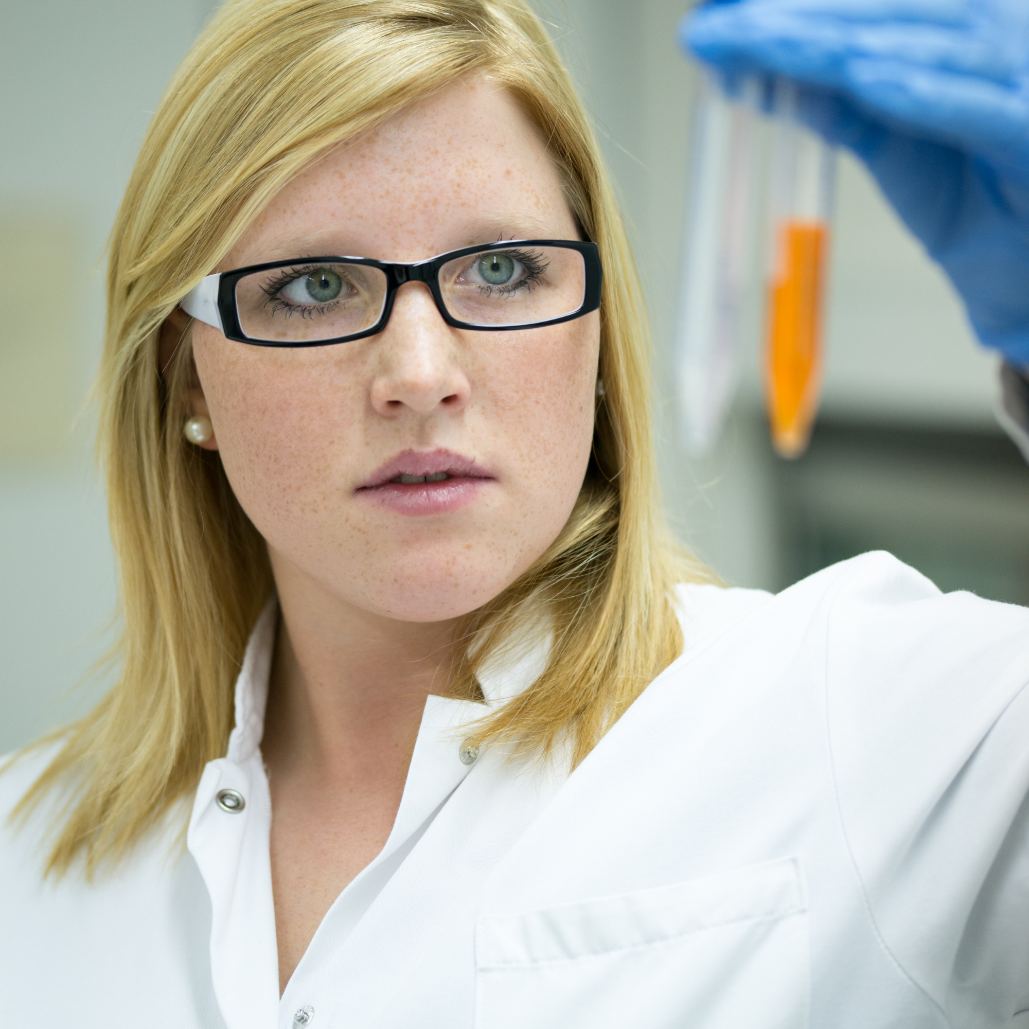 Scientist examining test tubes with orange liquid in a laboratory.