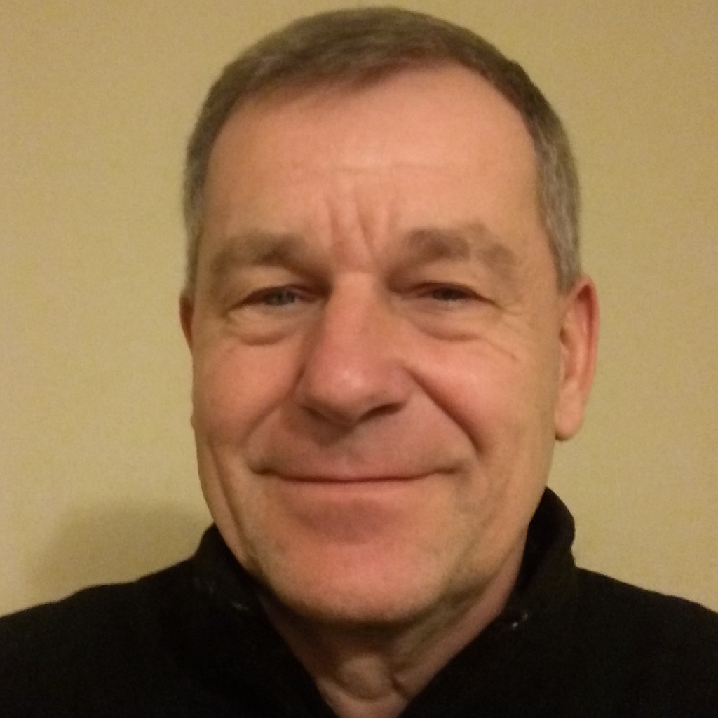 A man smiling in a close-up portrait against a plain background.