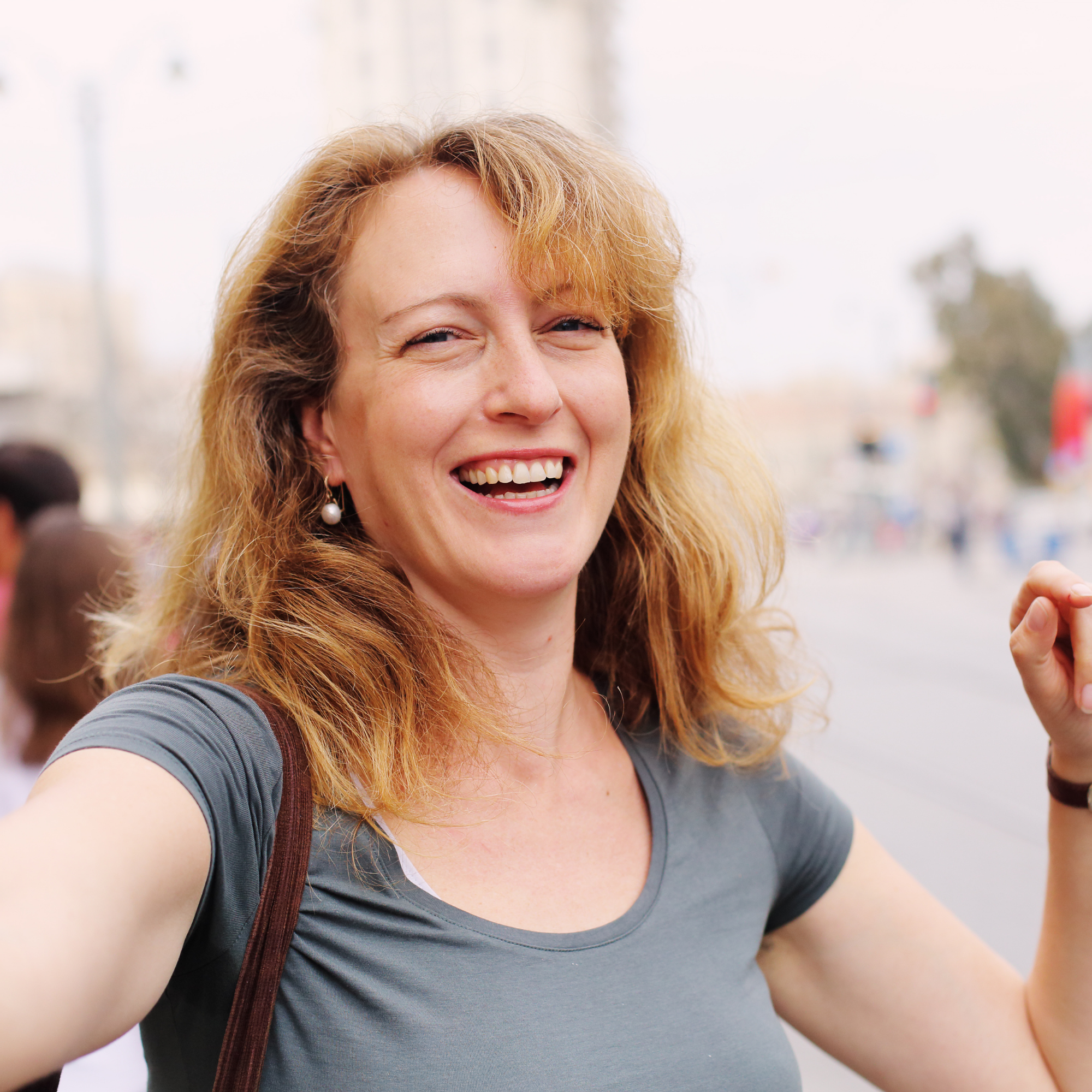 Smiling woman with long hair outdoors, wearing a gray shirt.