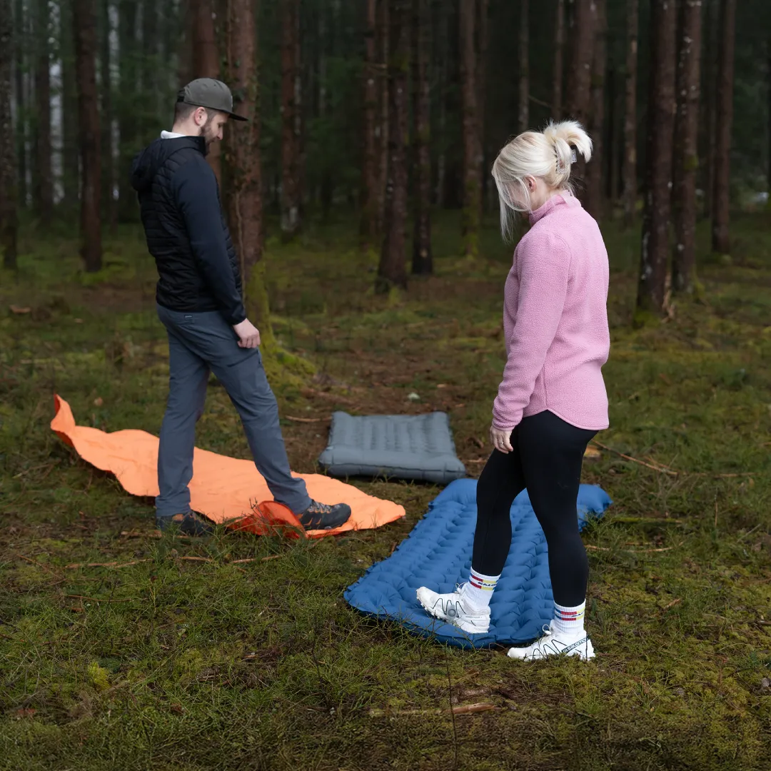 Two people setting up sleeping pads in a forest.