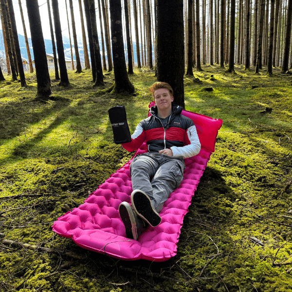 Person relaxing on a pink inflatable mattress in a forest.