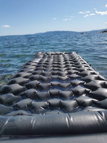 Inflatable mattress floating on a calm sea with distant mountains.