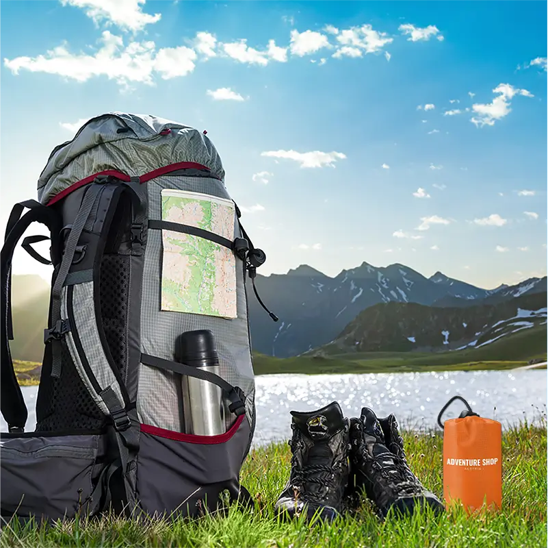 Backpack, boots, and gear on grass with mountains and lake in background.