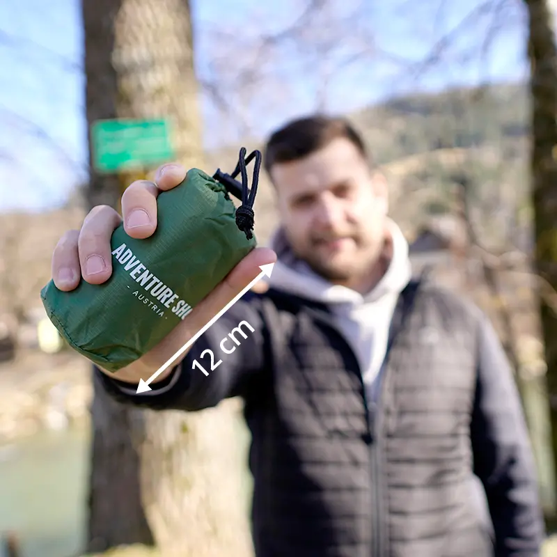 Person holding a small green bag labeled 'Adventure Shop' outdoors.
