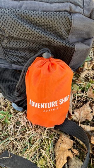 Orange bag labeled 'Adventure Shop Austria' next to a backpack on grass.
