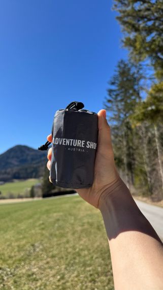 Hand holding a small bag labeled 'Adventure Shop Austria' outdoors.
