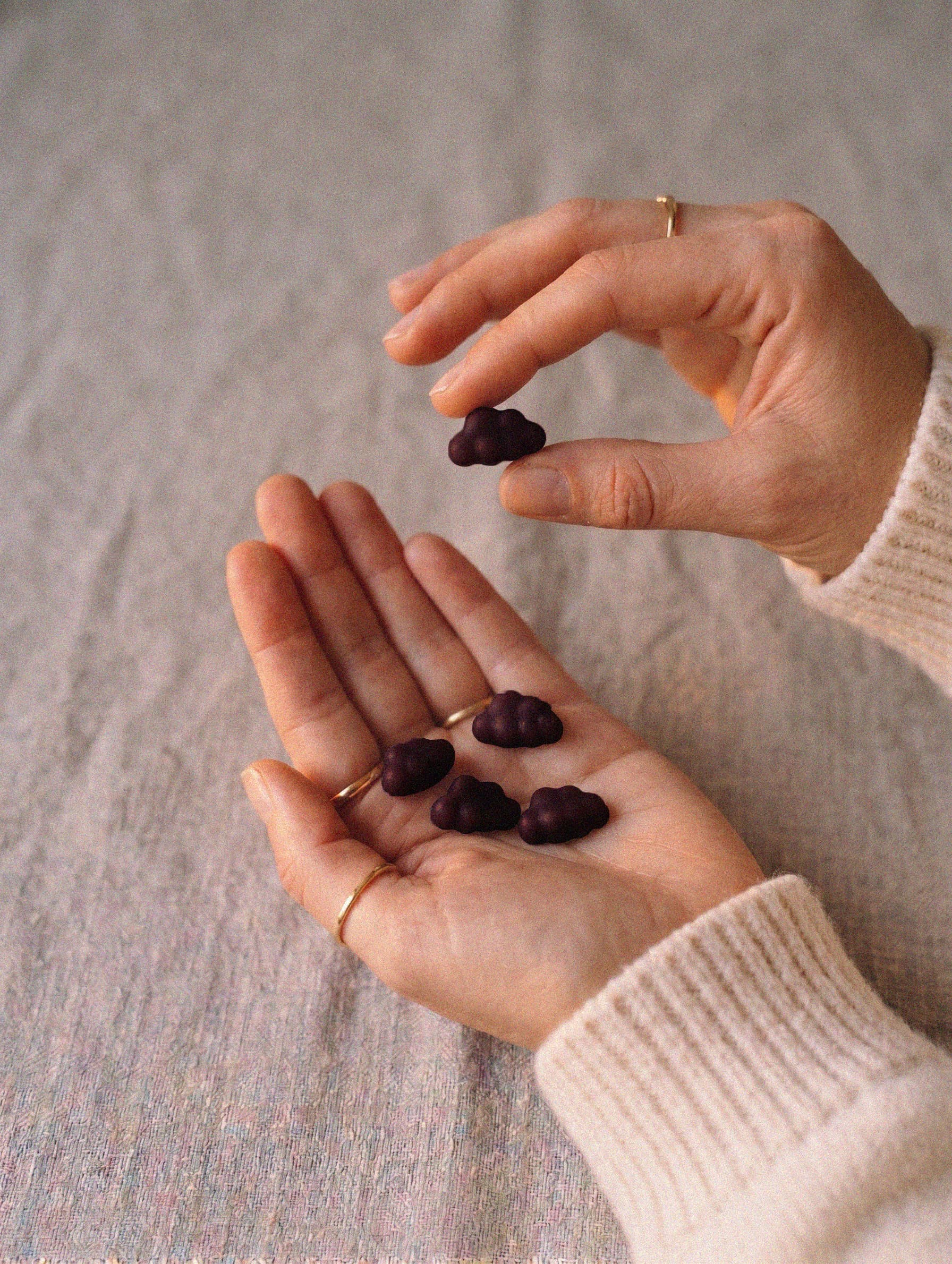 A person's hands holding several small, dark purple, cloud-shaped candies over a textured gray surface.
