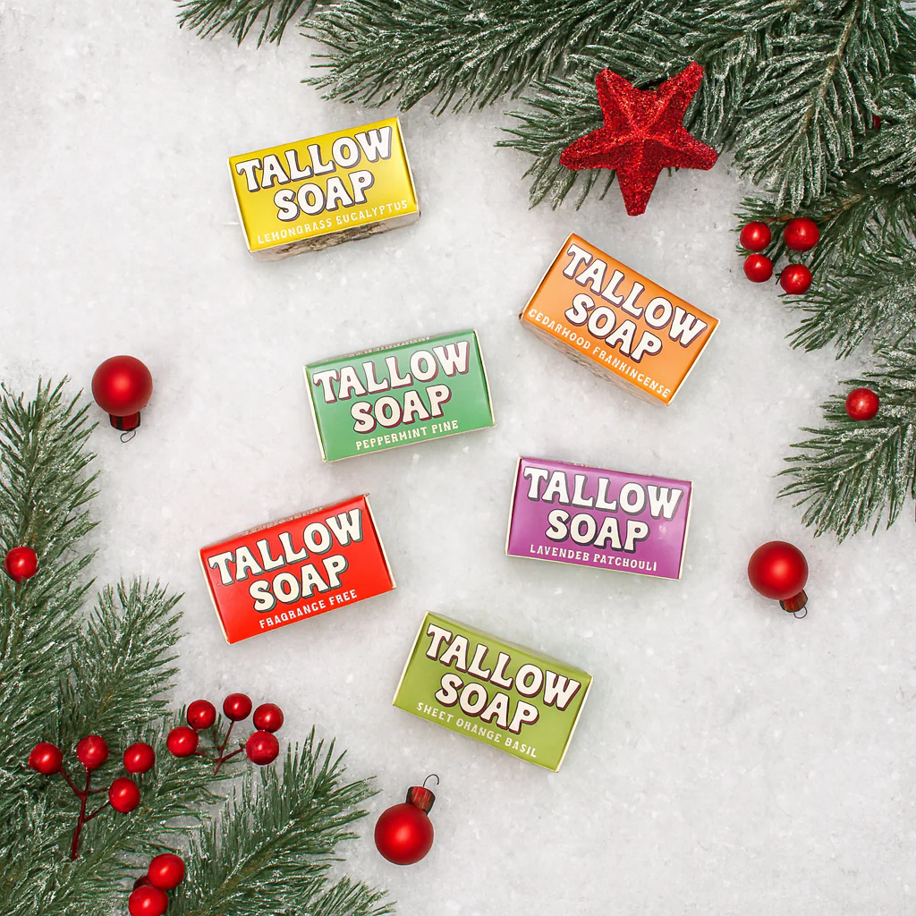Assorted tallow soap bars on snow with Christmas decorations and pine branches.