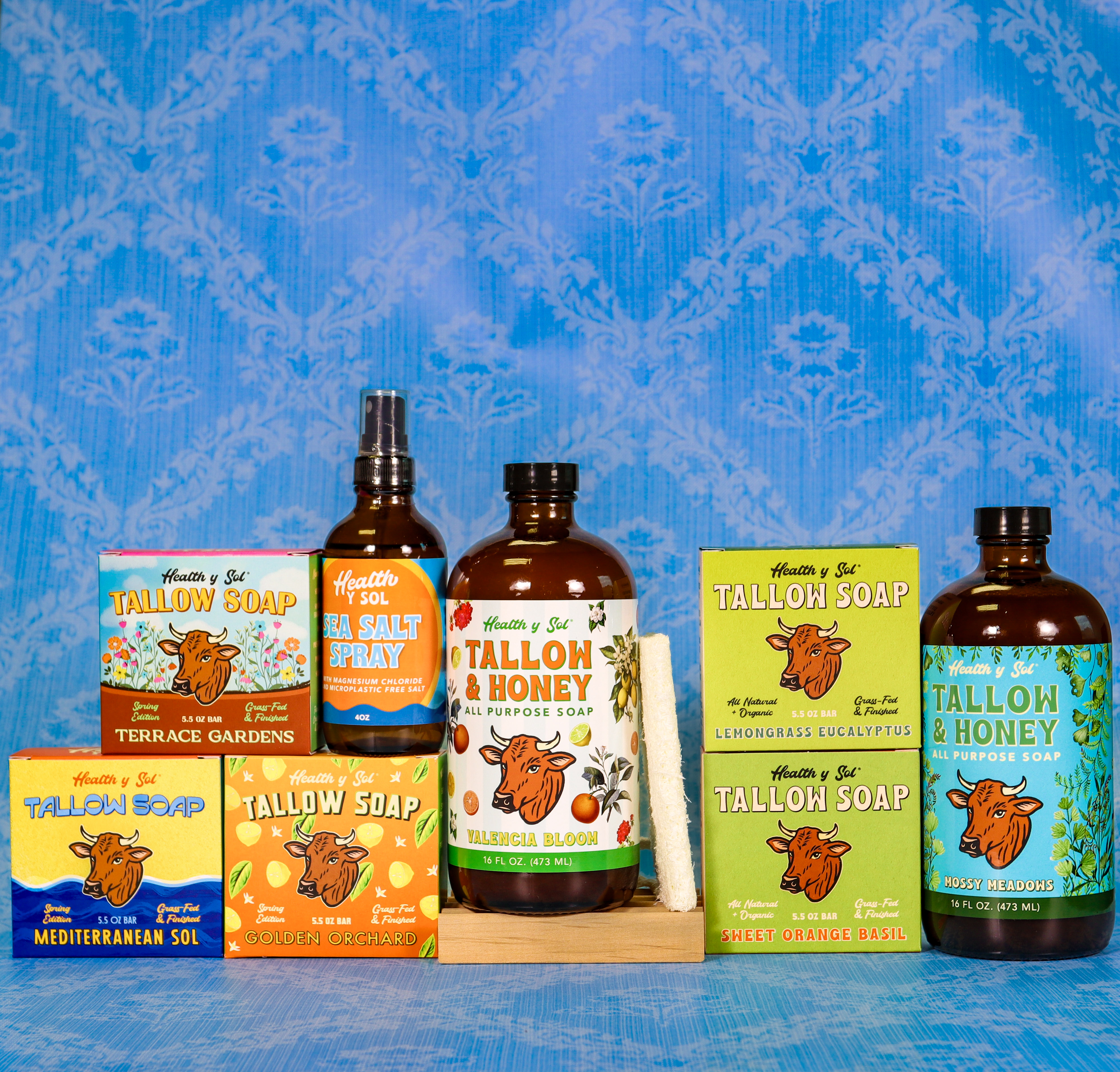 An assortment of Health y Sol brand tallow soap products in boxes and bottles against a blue background.