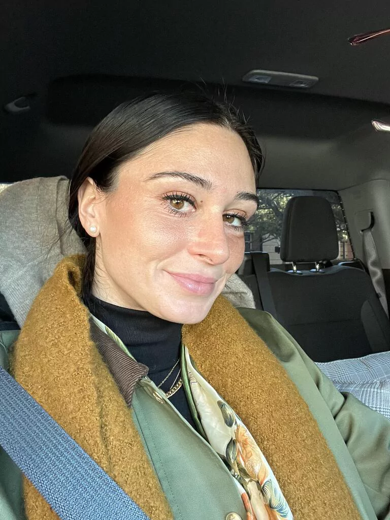 Person sitting in a car, wearing a green coat and brown scarf.