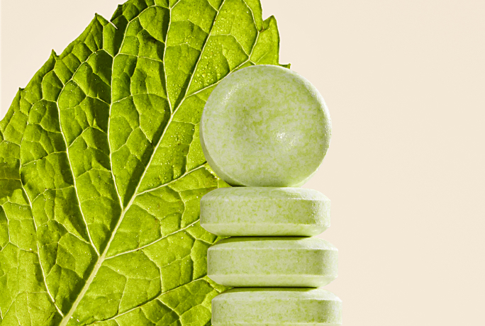 Green tablets stacked in front of a large green leaf.
