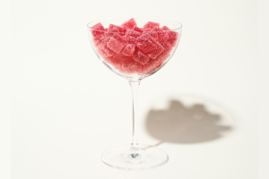 Glass filled with red sugar-coated gummy cubes on a white background.